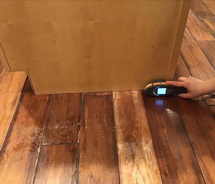 Wet hardwood floors with a moisture meter at the base of the cabinet.