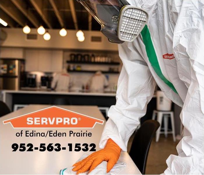 SERVPRO emplyoee wearing PPE and wiping a white table.