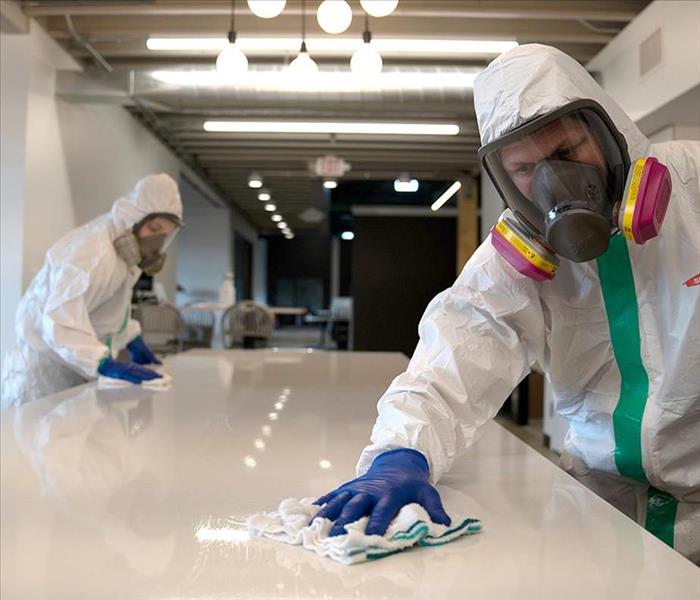 White office table being cleaned by 2 workers with white suits.